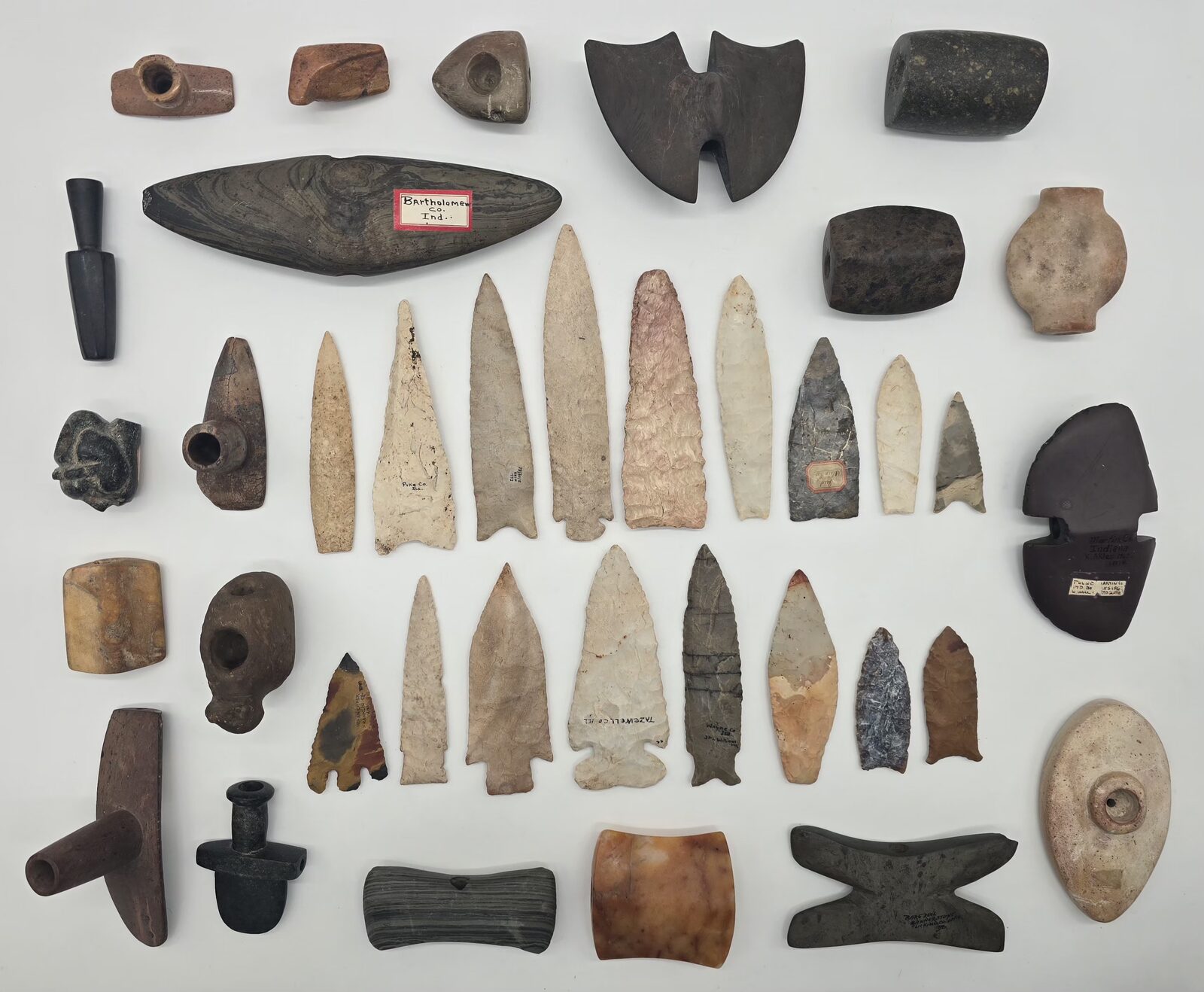 Flint points, stone pipes, bannerstones, and celts laid out on a white background